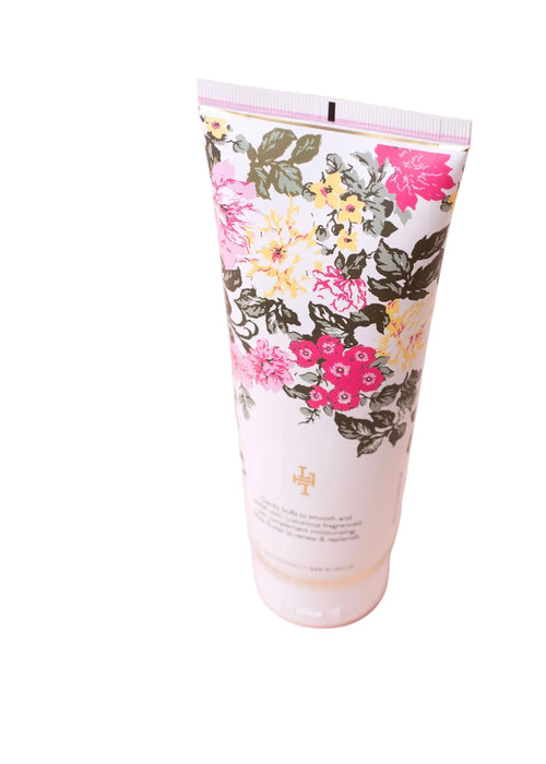 The Lollia Always in Rose Velvet Body Scrub by Margot Elena stands upright in a floral-patterned tube with pink, yellow, and green flowers on white—infused with nourishing botanicals for gentle exfoliation.
