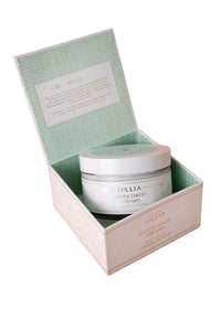 An open pastel green and white box reveals a round jar of Lollia Snowdrop Body Butter by Hampton Court Essential Luxuries & The Lavender Shop, labeled No. 32, on a pale pink background. The inner lid features a printed description.
