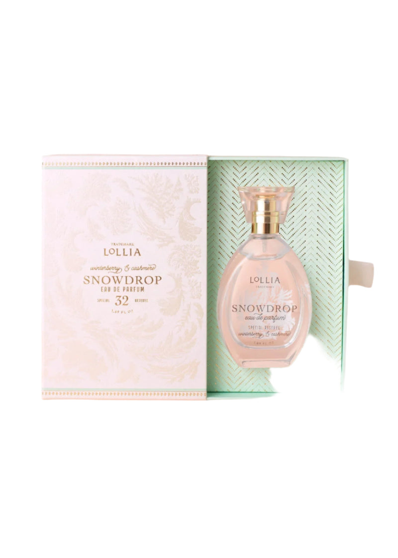 A Margot Elena Lollia Snowdrop Eau de Parfum bottle rests in an open, decorative light pink and green box with gold accents and textured floral patterns, evoking the delicate essence of winterberry and cashmere.
