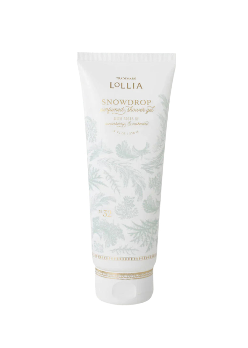 A white tube of Margot Elena's Lollia Snowdrop Perfumed Shower Gel, featuring pale leaf patterns and gold accents, stands upright against a plain white background.