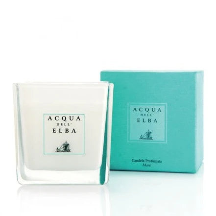 The Acqua dell'Elba Mare Scented Candle, in a glass holder, sits beside its turquoise box. Both display the Acqua dell'Elba logo with a sailboat, capturing the Mediterranean essence with lemon hints.