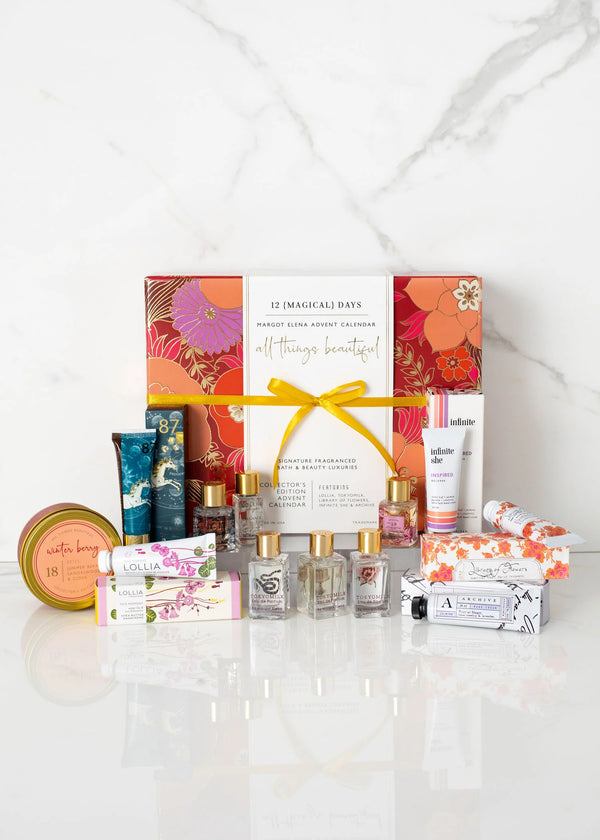 The Margot Elena Advent Calendar by Margot Elena—a colorful "12 Magical Days" gift box—rests on a white surface, surrounded by lotions, candles, perfumes, creams, and soaps. It's the perfect treat for any fragrance lover.