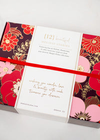 A decorative box adorned with floral designs in red, pink, and gold. A white band with text in elegant gold and red font wraps around the box, reading: "Margot Elena Advent Calendar" by Margot Elena and "wishing you wonder, love & beauty with each treasure you discover.