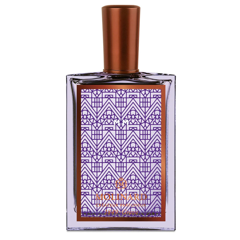 Molinard MM Eau de Parfum by Molinard comes in a clear glass bottle with a bronze cap and a label featuring geometric purple and bronze Art Deco patterns, illustrating the elegance of this woody amber fragrance.
