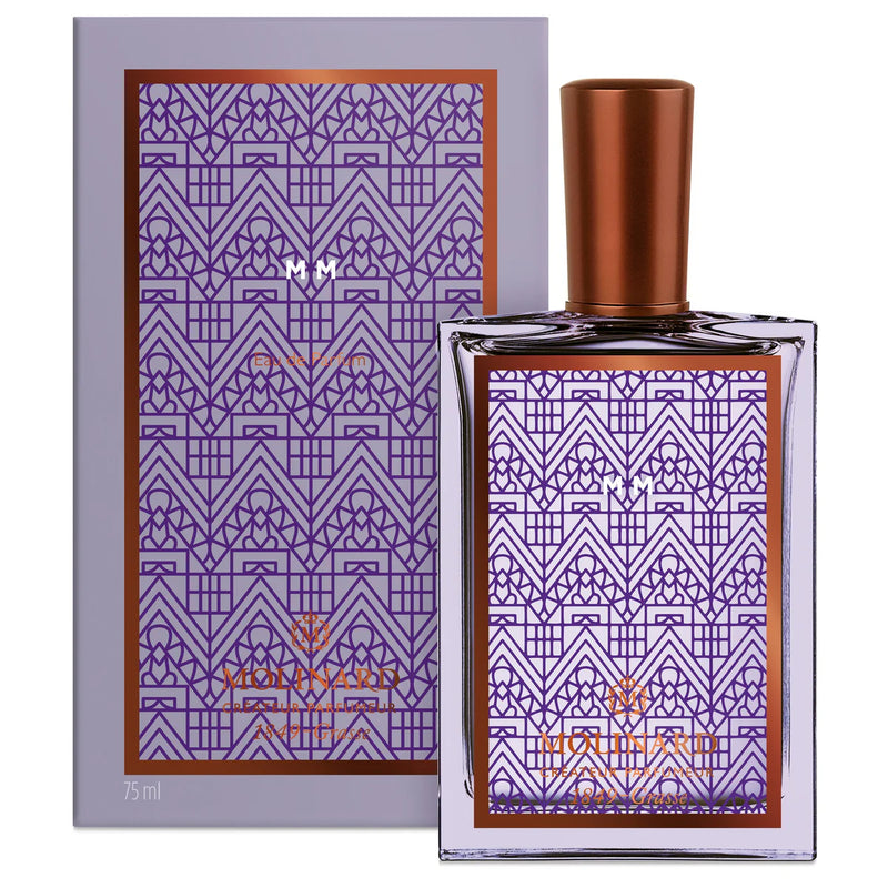 A 75 ml rectangular Molinard MM Eau de Parfum bottle for men, featuring a copper cap and art deco purple-copper geometric pattern, stands before a matching box. This woody amber fragrance is by Molinard.