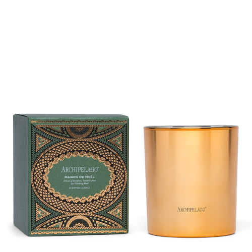 A decorative green box labeled "Archipelago Maison de Noel Credenza Candle" by Archipelago Botanicals sits beside a shiny gold holiday candle holder, both displayed against a white background.