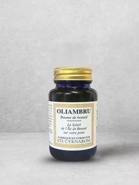 A dark glass jar with a gold lid labeled "Oliambru Beauty Balm" by ISULA parfums. Made in Corsica with natural organic oils, the French-labeled jar rests on a light gray background.