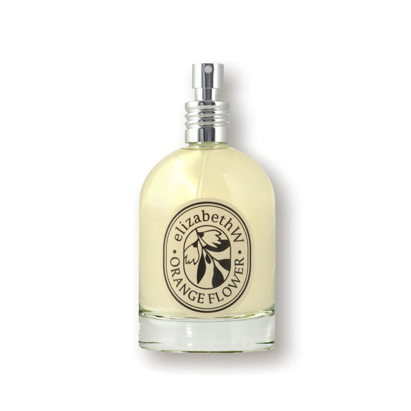 A clear glass bottle with a silver spray holds light yellow Elizabeth W Orange Flower Eau de Parfum, a floral fragrance from elizabeth W. The label highlights this signature orange flower scent in their eau de parfum collection.