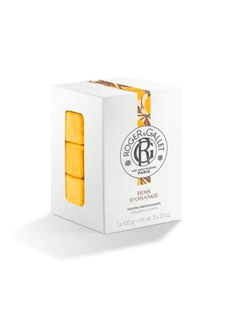 A white box of Roger & Gallet Orange Wood Wellbeing Soaps Set (3 x 3.5 oz) displays the logo and front label, with a window showing three vibrant orange artisanal soap bars stacked inside.