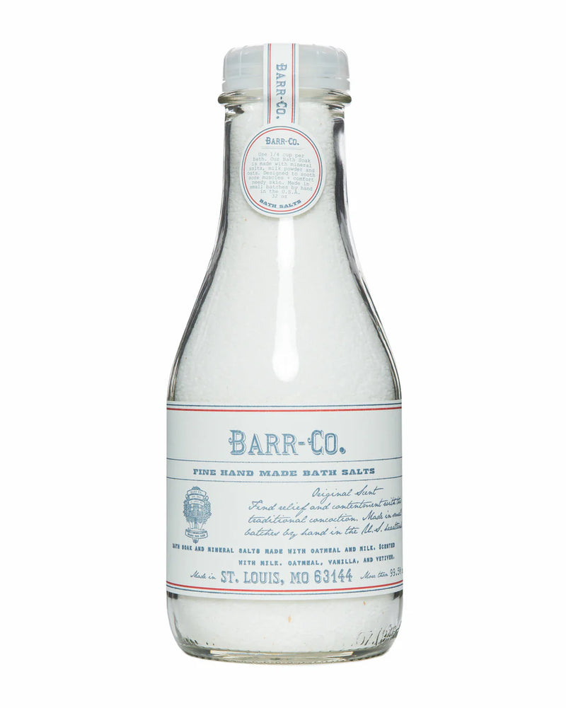 A clear glass bottle with a white and blue label and matching cap, labeled "Barr-Co. Original Scent Bath Soak Salt," contains white mineral bath salts made by Barr-Co. The label features product details and origin information.