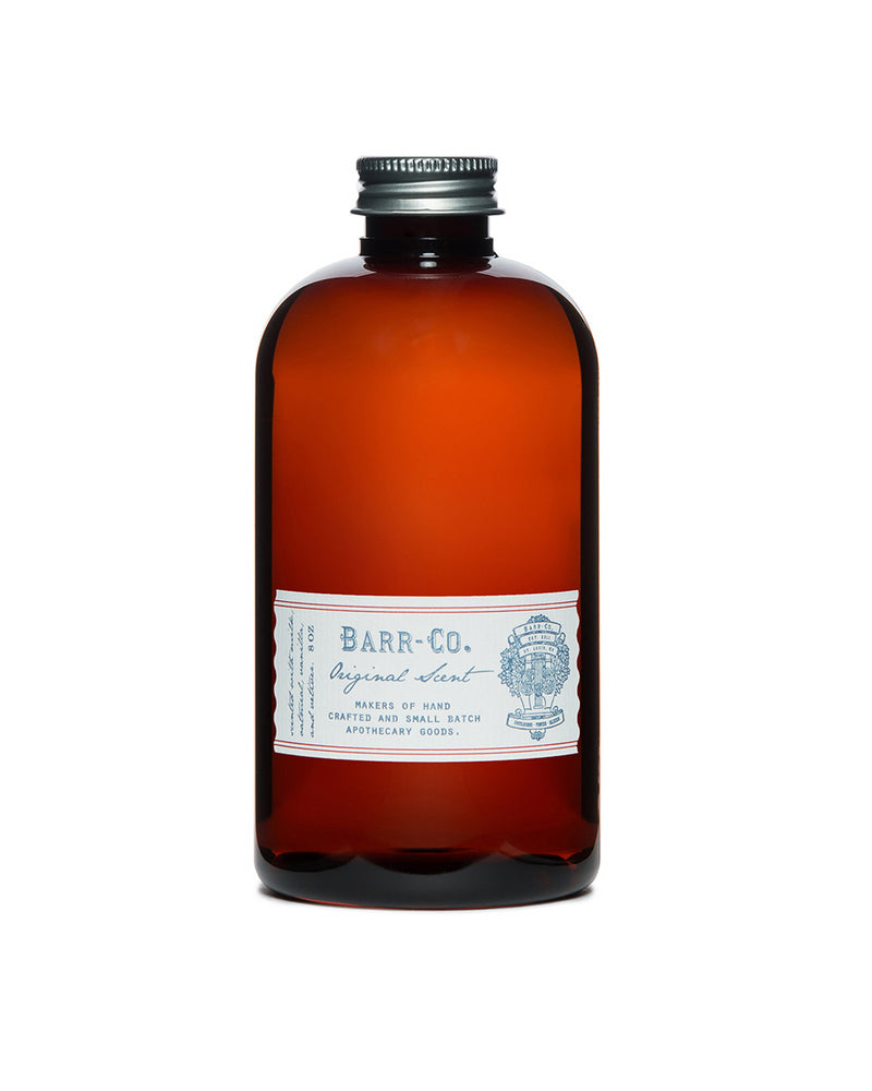 A nostalgic amber bottle with a metal screw cap, featuring Barr-Co.'s emblematic white label with blue text, hints at the luxurious hand-crafted apothecary diffuser oil inside, labeled "Barr-Co. Original Scent Diffuser Oil Refill," to elevate any space.