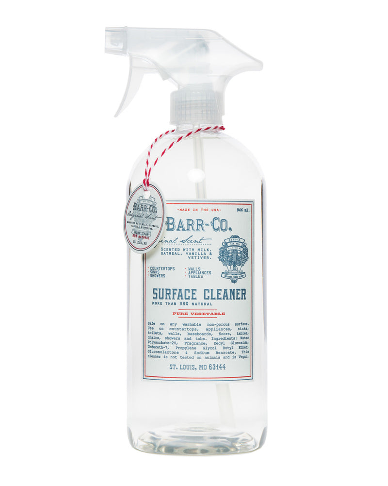 Clear spray bottle of Barr-Co. Original Scent Surface Cleaner with a white label that includes decorative text and details. A red and white twine is tied around the neck of the bottle by Barr-Co.