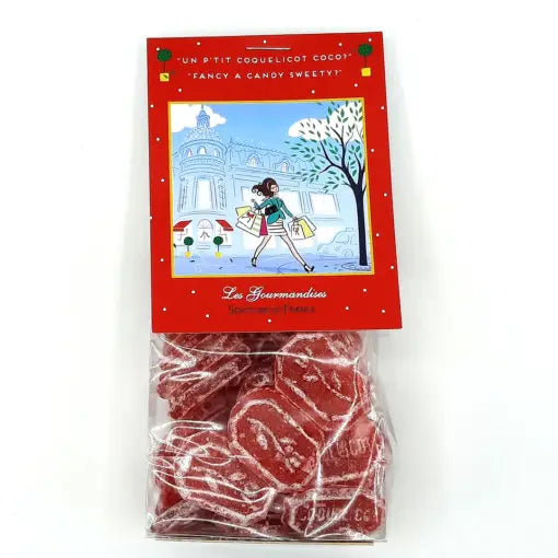 A bag of "Senteurs De France Versailles Poppies Candies in Paris Theme" is shown. The red, poppy-shaped sweets are designed as various objects. The label features a cartoon illustration of a woman carrying shopping bags in front of a French-styled building, with text in both English and French.