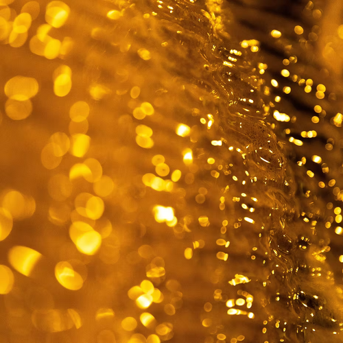Close-up of golden yellow bokeh lights and reflections, creating an abstract background that evokes the warmth and richness of ISULA parfums Ambra Preziosa - Precious Amber eau de toilette.