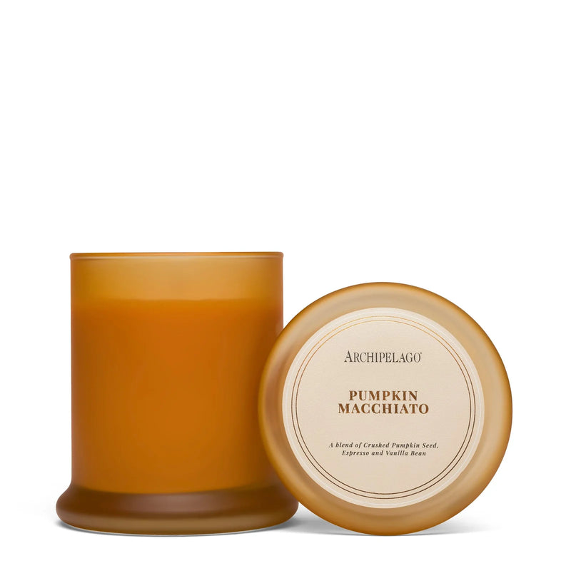 A brown glass Archipelago Botanicals Pumpkin Macchiato Jar Candle - Ltd Edition sits with its lid beside it. The label describes this autumn scent as a blend of pumpkin seed, espresso, and vanilla bean.