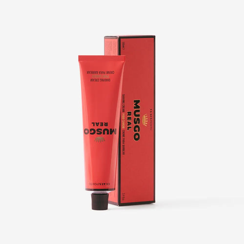 A red tube of Claus Porto Musgo Real Puro Sangue Shaving Cream by Claus Porto 1887 stands upright before its matching box, both labeled with product details. The lanolin cream offers a woody-leathery scent. The background is plain white.