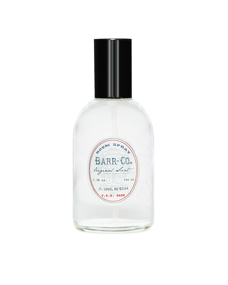 A clear glass bottle labeled "K. Hall Barr-Co. Original Scent Room Spray" contains a transparent liquid. The bottle features a black pump nozzle and a white label with red and blue text, including the brand name and location, "St. Louis, MO 63104," indicating it is made in the USA. Perfect as a room spray with hints of vanilla.
