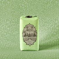 A bar of Claus Porto 1887 Classico Spring Lettuce Soap, wrapped in light green paper with white polka dots, features an ornate black-and-white vintage label showcasing pistachio nut seed oil and a scenic illustration with decorative text.
