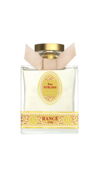 Rancé Sublime Eau de Parfum by Rancé comes in a square glass bottle with a gold cap and beige ribbon, adorned with yellow ornate details that echo the refined elegance of its floral fragrance.