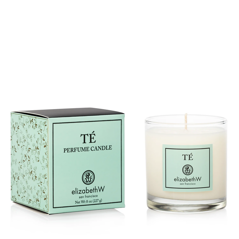 A elizabeth W Signature Té Candle by elizabeth W displayed next to its packaging. The candle is in a clear glass with a single wick, and the box is mint green with decorative patterns.