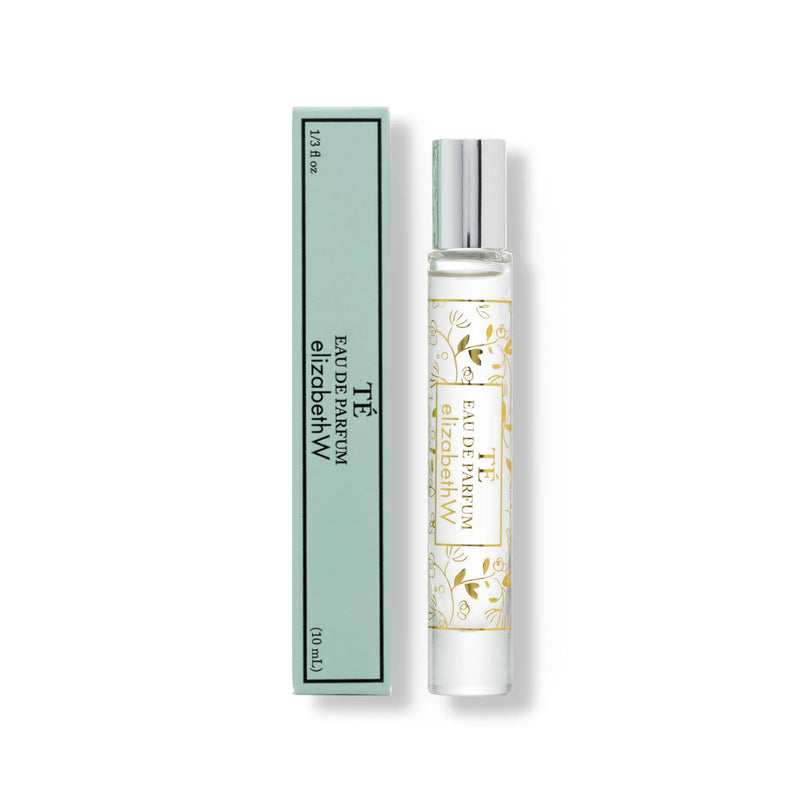 A elizabeth W Signature Té Rollerball bottle next to its mint green packaging box. The bottle has a white label with gold floral patterns and text that reads "Eau de Parfum.