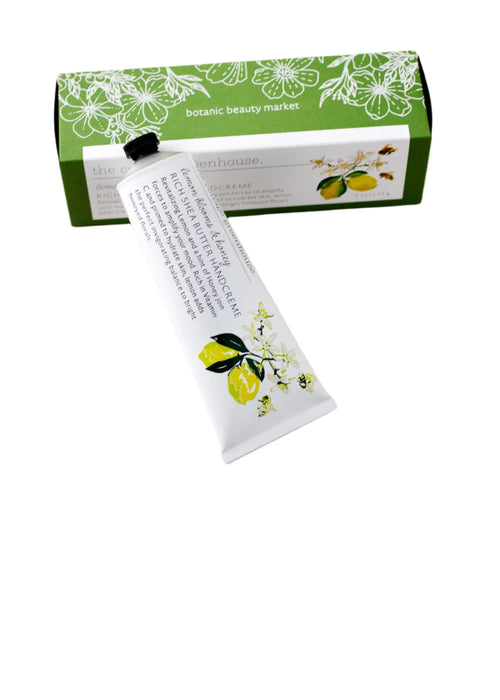 A tube of "The Cottage Greenhouse Lemon Blooms & Honey Handcreme" by Margot Elena, featuring a floral design with green leaves, peeks out of its box labeled "Botanic Beauty Market," infused with nourishing avocado oil.