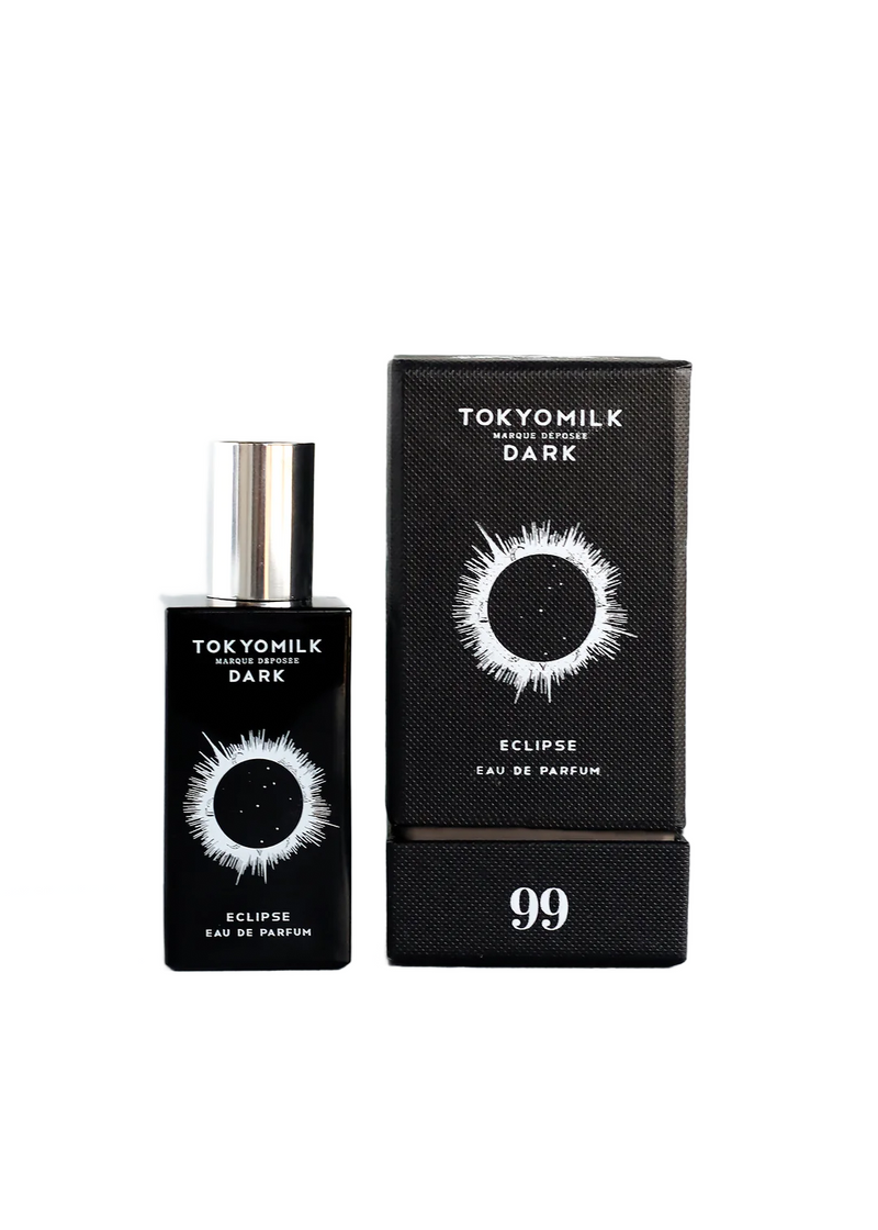A bottle of Margot Elena's TokyoMilk Dark Eclipse No. 99 Eau de Parfum perfume next to its packaging. The bottle and box are black with a white graphic of an eye with rays, labeled "Eau de Par.