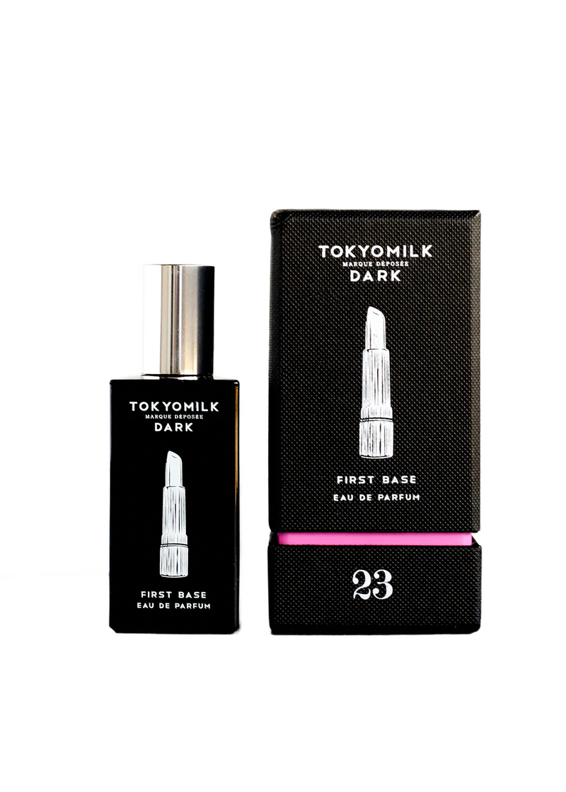 Black glass perfume bottle labeled "Margot Elena TokyoMilk Dark First Base No. 23 Eau De Parfum" next to its textured box with a pink accent and Cedarwood note, number 23 displayed prominently.