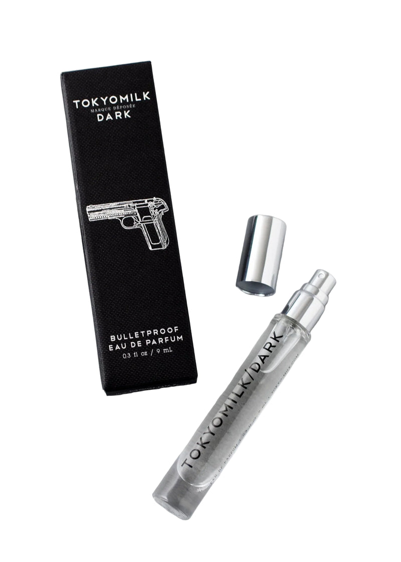 The Margot Elena TokyoMilk Dark Bulletproof Travel Eau De Parfum comes in a silver-capped spray bottle beside its black box with a handgun line drawing—a daring unisex scent for your collection.