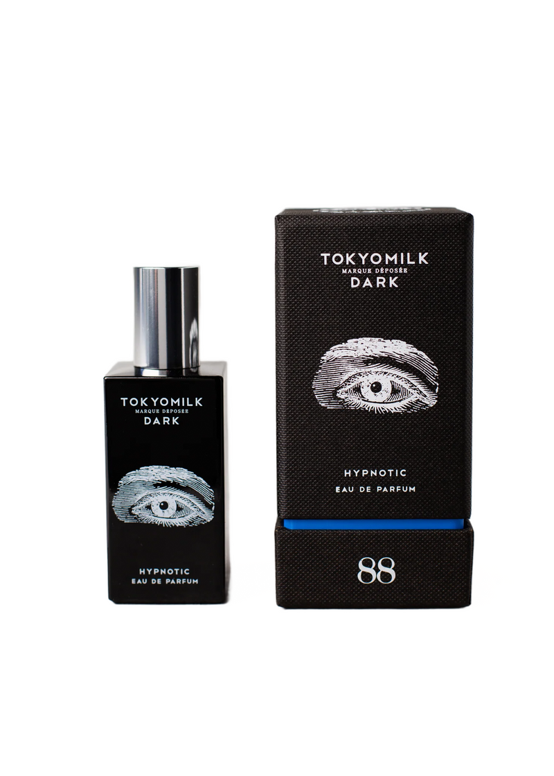A bottle of Margot Elena's TokyoMilk Dark Hypnotic Eau de Parfum next to its packaging box. The box and bottle are black with an eye design and the text "Hypnotic".