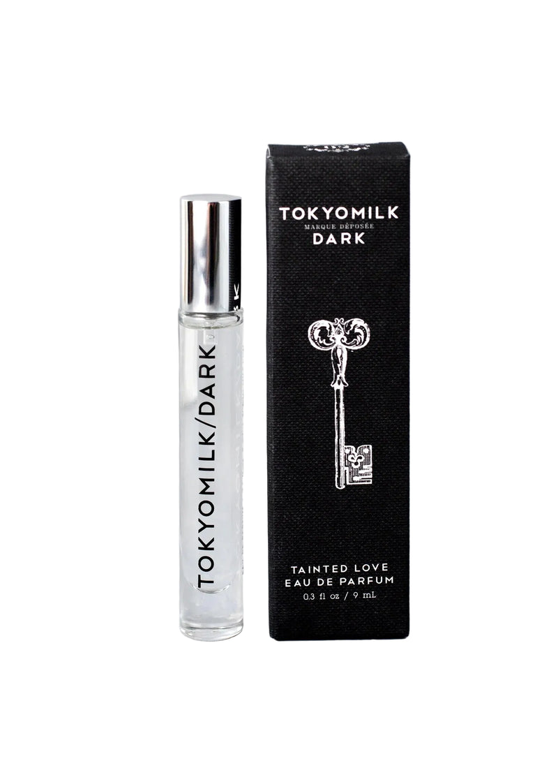 The Margot Elena TokyoMilk Dark Tainted Love Travel Eau De Parfum features dark vanilla bean in a clear bottle with a silver cap and black lettering, displayed beside its black box packaging with a vintage key illustration and bold white text.