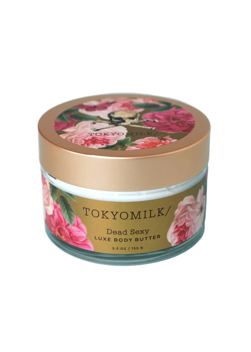 A round jar of Margot Elena's TokyoMilk Dead Sexy Body Butter features a gold lid and floral design with pink and red flowers. The label displays the product name and 5.5 oz (155 g) net weight, offering luxurious, intensive moisture.