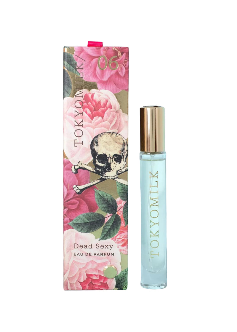 The Margot Elena TokyoMilk Dead Sexy Travel Spray comes in a clear bottle with a gold cap and vertical TOKYOMILK branding, housed in a floral box with pink flowers, green leaves, and a skull with crossbones—ideal for travel.