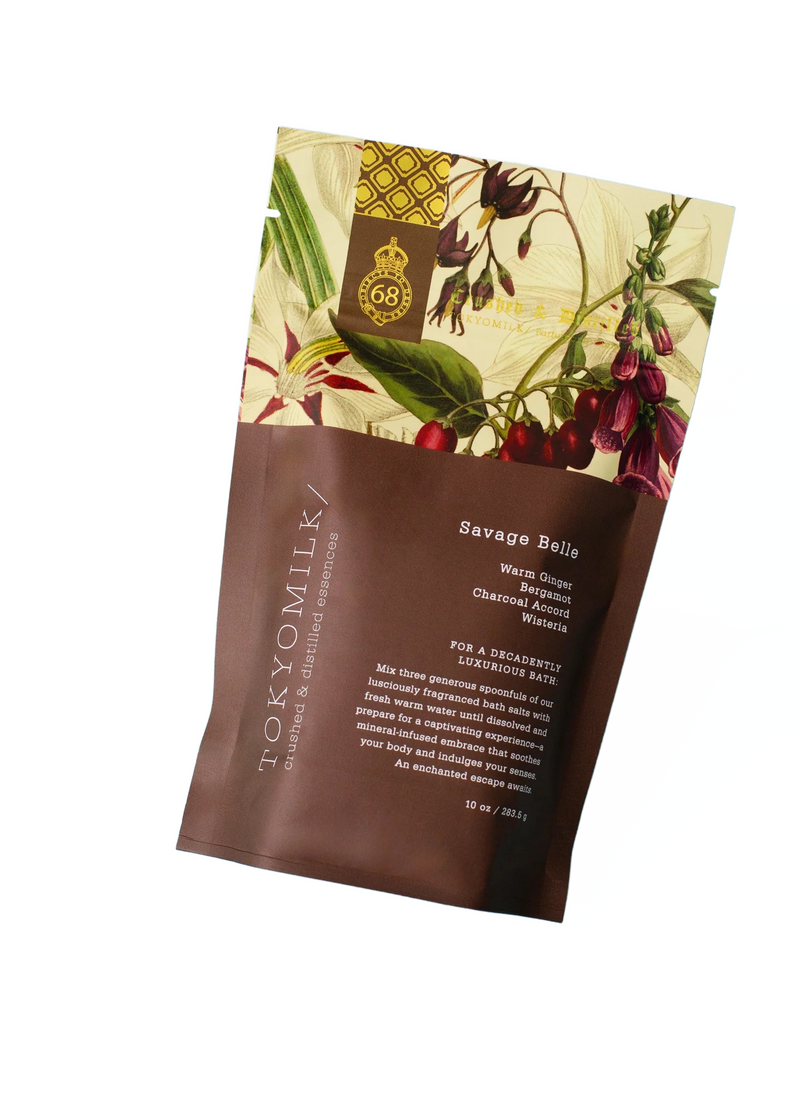 A colorful Margot Elena TokyoMilk Savage Belle Salt Soak packaging featuring luxurious illustrations of botanicals and birds on a cream background, transitioning to solid brown below with elegant text.