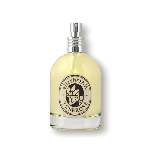 A transparent bottle of elizabeth W Botanist's Scent Lab Tuberose Eau de Parfum with a metallic spray nozzle. The bottle contains light yellow liquid and has an oval label featuring the brand name "elizabeth W" and the word "TUBEROSE," along with a floral design, hinting at its luxurious scent.