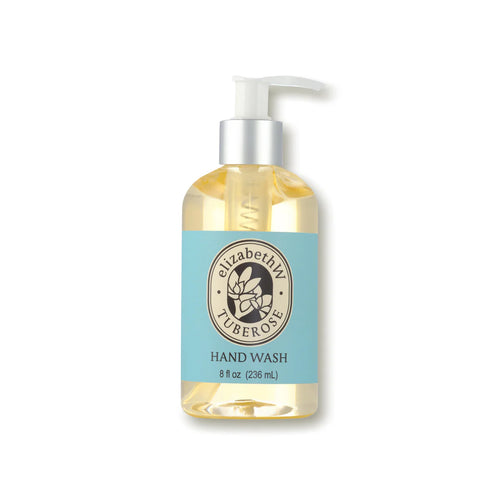 A clear pump bottle from elizabeth W features a label reading "Botanist's Scent Lab Tuberose Hand Wash," showcasing light blue text. The bottle contains light yellow liquid soap and has an 8 fl oz (236 mL) capacity marked. A circular logo with a white floral illustration is also displayed on the label.