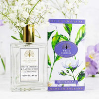 A clear perfume bottle labeled "The English Soap Co. White Jasmine Eau de Toilette" stands next to its floral-patterned box with gold and purple accents. This cruelty-free scent, made in England, is surrounded by white flowers.