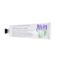 A white tube of "The Cottage Greenhouse Wild Lavender & Violet Handcreme" by Margot Elena, adorned with lavender flower illustrations. It’s infused with rich shea butter and nourishing avocado oil, labeled "Rich Shea Butter Handcreme.