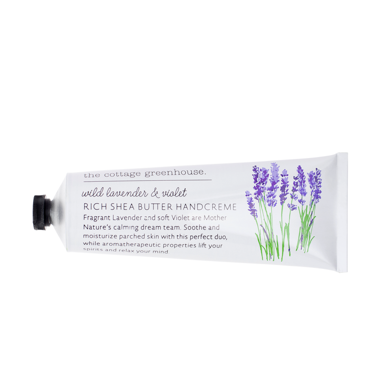 A white tube of "The Cottage Greenhouse Wild Lavender & Violet Handcreme" by Margot Elena, adorned with lavender flower illustrations. It’s infused with rich shea butter and nourishing avocado oil, labeled "Rich Shea Butter Handcreme.