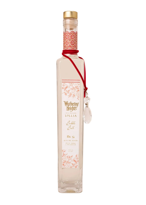 A tall, clear glass bottle with a gold cap and floral "WUTHERING HEIGHTS" label by Margot Elena, accented with a red ribbon and crystal pendant—beautiful next to your Lollia 'WUTHERING HEIGHTS' Kiss Me Again Bubble Bath.