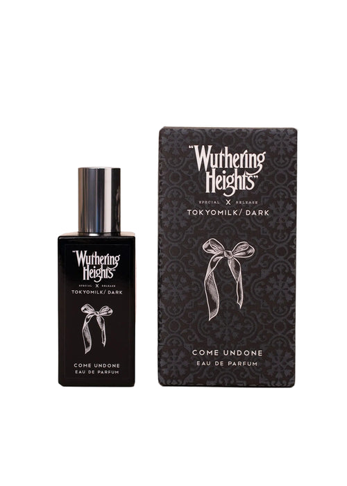 A black perfume bottle and its box, both from Margot Elena's TokyoMilk Dark "WUTHERING HEIGHTS" Come Undone Eau De Parfum, feature a white ribbon design on a patterned dark background.