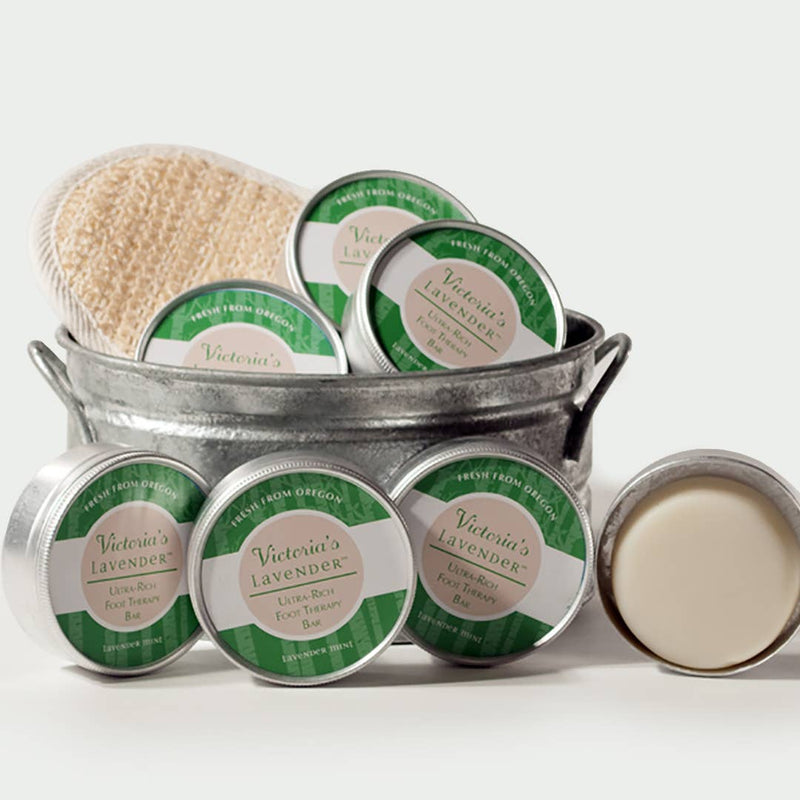 Metal tub containing multiple tins of Victoria's Lavender - Lavender Mint Foot Therapy Lotion Bar and a brush, set against a white background. One tin is open, displaying the moisturizing balm inside.