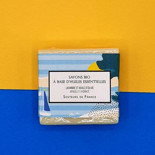 A pack of Senteurs De France Lavender Organic Soap labeled in French, featuring a blue and white striped design with illustrations of lavender essential oil, set against a contrasting yellow and blue background.