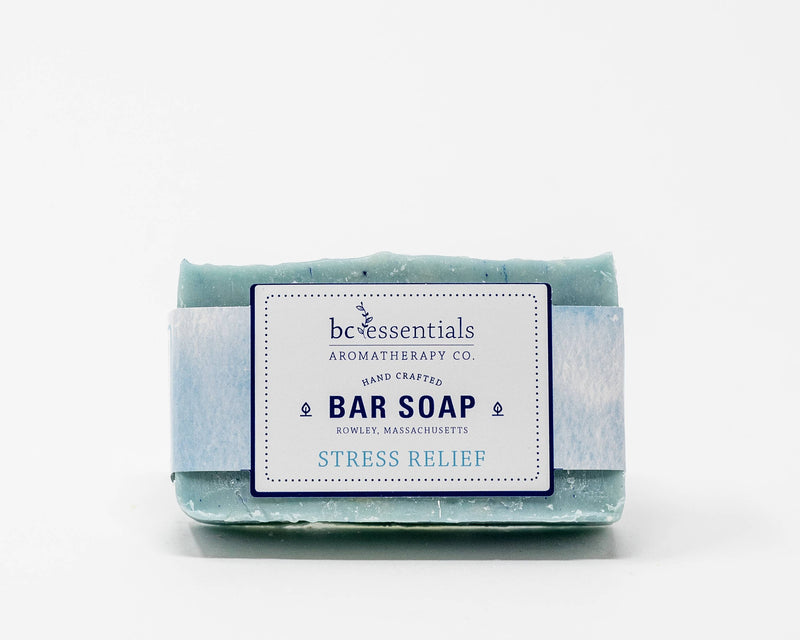 A bar of BC Essentials - Stress Relief Bar Soap with a white label that reads "BC Essentials Aromatherapy, Stress Relief" from Rowley, Massachusetts. The soap has a textured surface and rests against a white background.