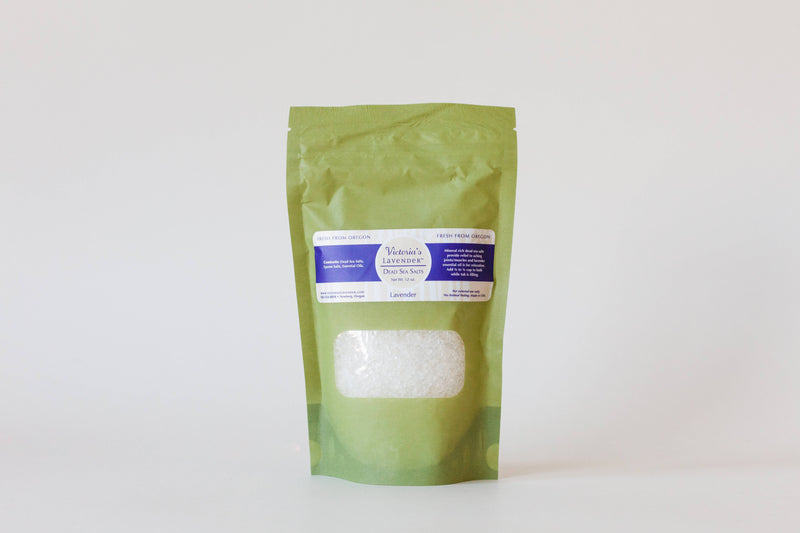 Green packaging with a clear window showing white bath salts infused with Lavender Essential Oil from Victoria's Lavender, labeled "Victoria's Lavender Dead Sea Bath Salt", standing on a plain white background.