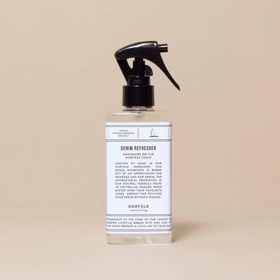 A spray bottle labeled "Norfolk Natural Living Coastal Denim Refresher" against a neutral beige background. The label features care instructions and branding details in a simple, elegant font.