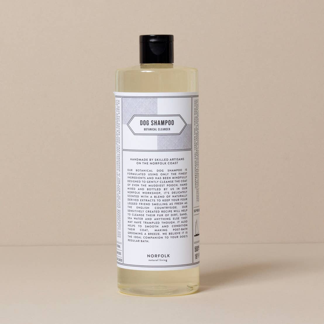 A bottle of Norfolk Natural Living Spring 91 Dog Shampoo labeled "dog shampoo fragrance-free with coconut oil" in a minimalist design against a beige background. The label is detailed with text about the product attributes.
