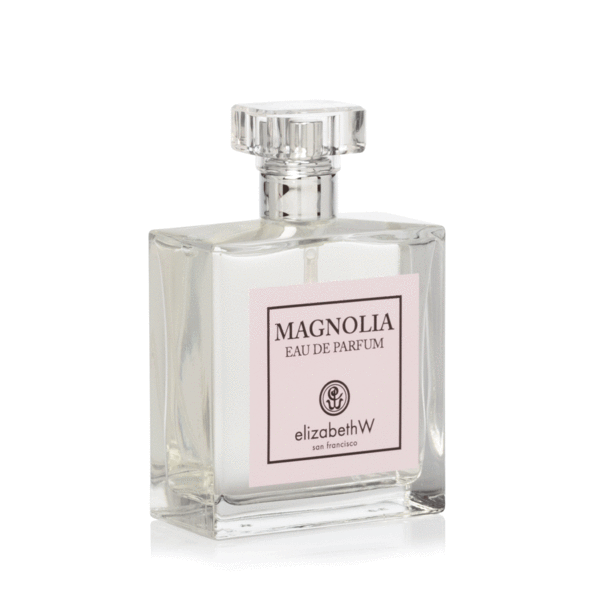 A clear glass perfume bottle with a square base and a faceted cap, labeled "elizabeth W Signature Magnolia Eau de Parfum by elizabeth W San Francisco" on a pink and white label.