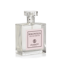 A clear glass perfume bottle with a square base and a faceted cap, labeled "elizabeth W Signature Magnolia Eau de Parfum by elizabeth W San Francisco" on a pink and white label.