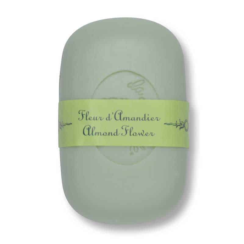 A bar of luxurious soap in a pale green color wrapped with a light green paper band labeled "La Lavande Almond Flower" in decorative script.